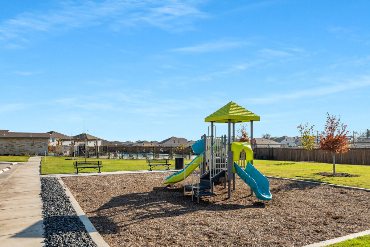 View of tot lot and playground with pool and amenity center in the background.