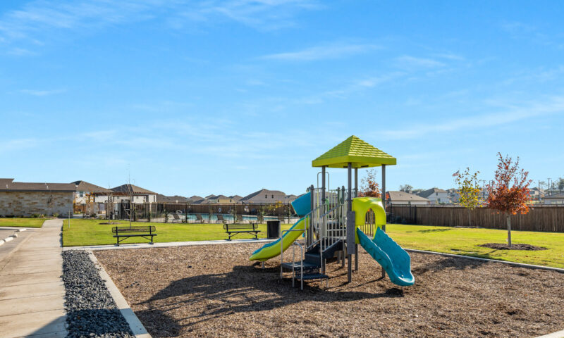 View of tot lot and playground with pool and amenity center in the background.