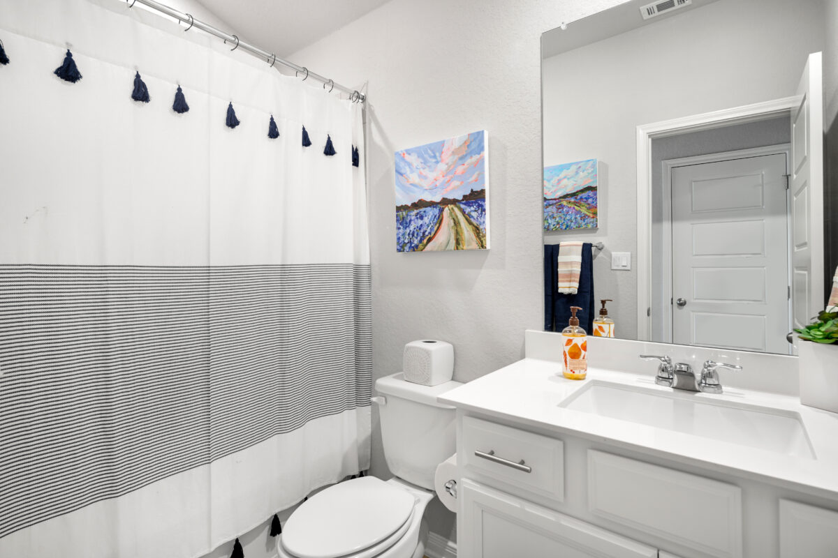 Close-up view of secondary bathroom showing shower curtain, toilet and vanity area.