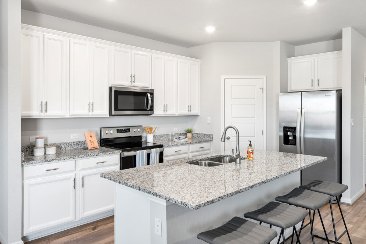 View of kitchen with white cabinets, granite countertops, gray stools, and stainless steel appliances.