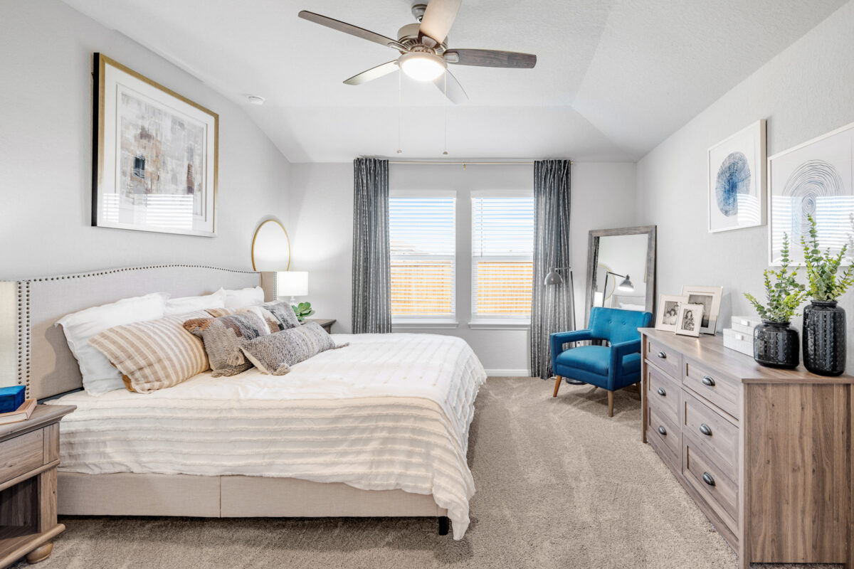 Main bedroom furnished with bed, blue chair, and dresser.