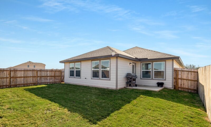 View of fully fenced backyard, green grass, and patio area.