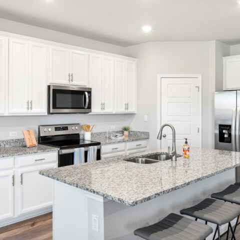 View of kitchen with white cabinets, granite countertops, gray stools, and stainless steel appliances.