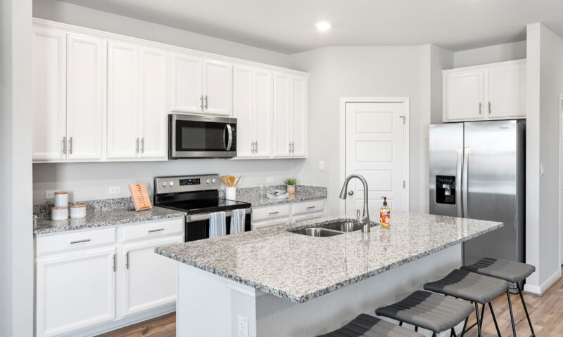 View of kitchen with white cabinets, granite countertops, gray stools, and stainless steel appliances.