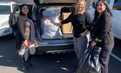 Three women loading bags of clothing into the back of a car.