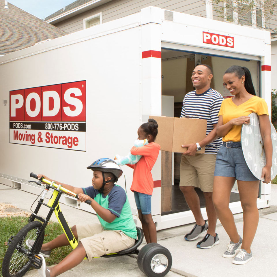 Family of four standing in front of portable storage container unloading items.