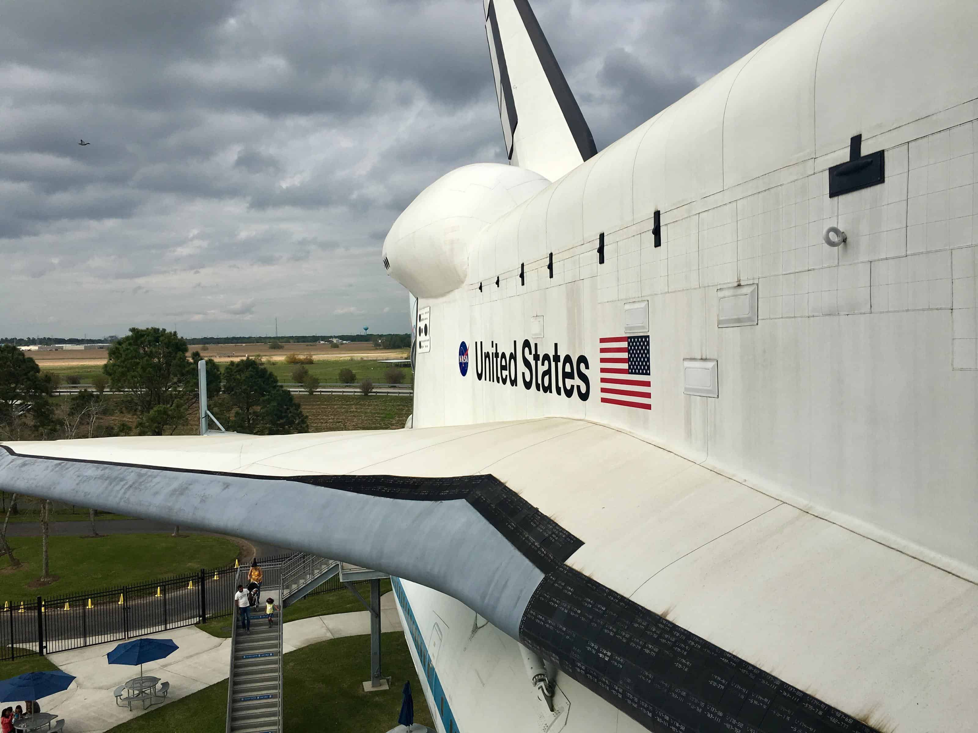 Side view of wing of stationary US Space Shuttle with ominous grey skies in background.