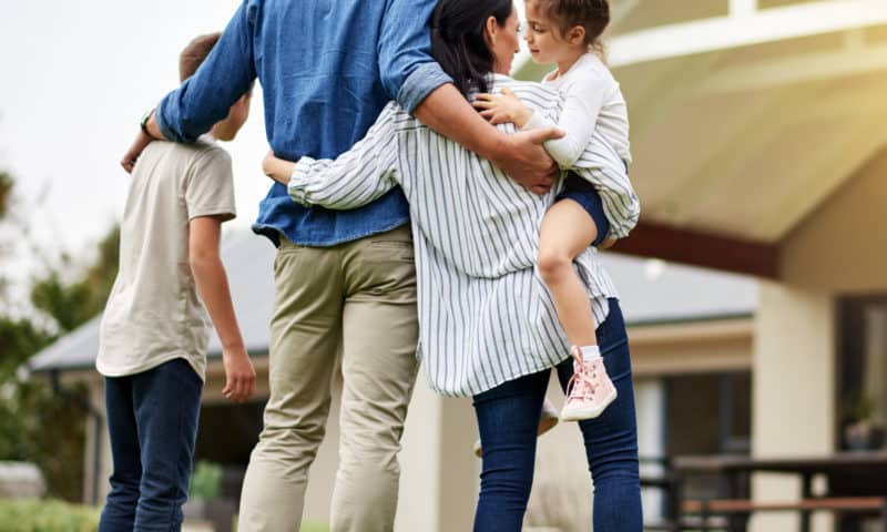 A family of four embracing in front of a house.