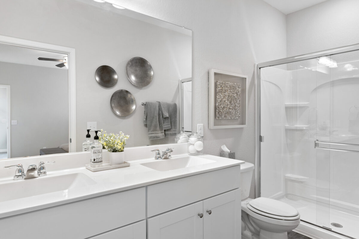 View of staged main bathroom with dual sinks and shower.