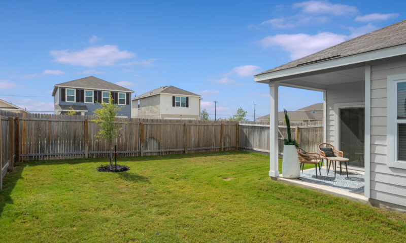 View of home with fully fenced backyard, patio seating for two in the Trails at Culebra community.