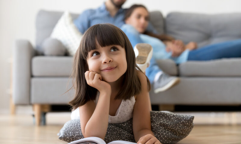 Daughter dreaming lying on warm floor with book at home