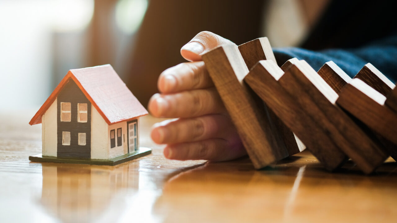 Close-up Of Business Woman Hand Stopping and Covering The Wooden Blocks From Falling On House Model, insurance concept.