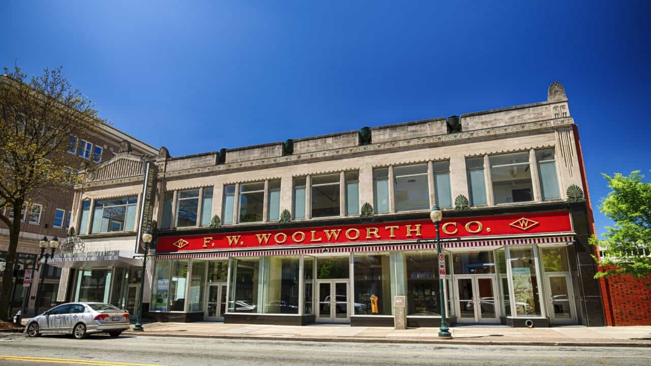 Street-level view of two-story building with tall windows and red and gold sign.