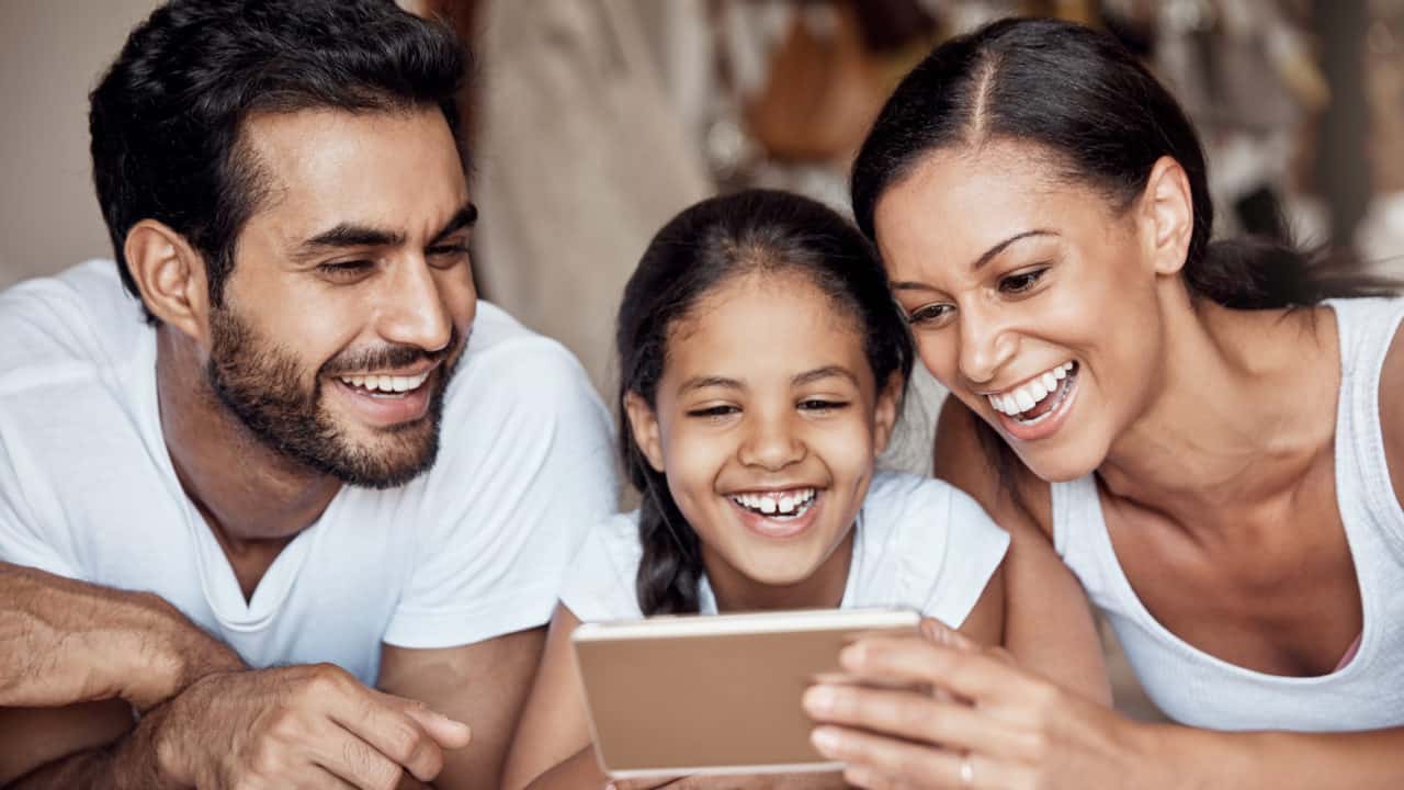 A man and woman with a young girl between them using a cellphone together.