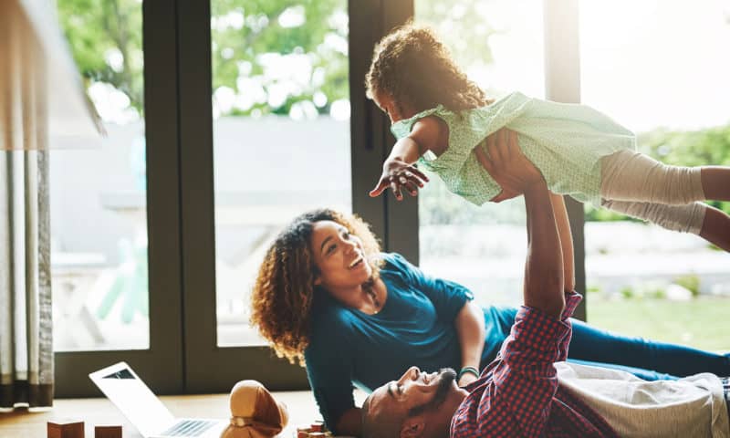 Young father and mother lying on the ground, the father is lifting up his daughter in air.