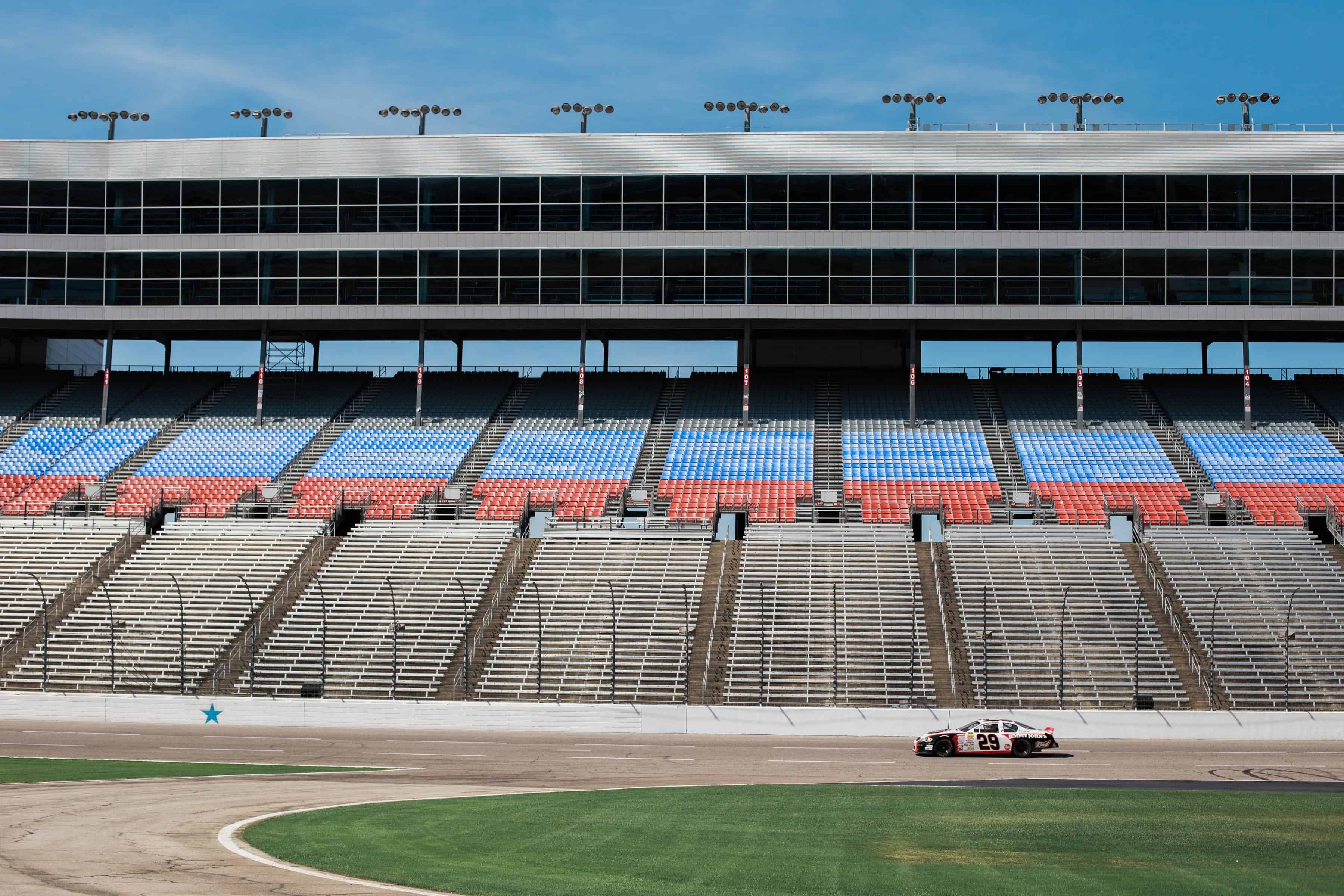 View of race way track, single race car and empty spectator seats.
