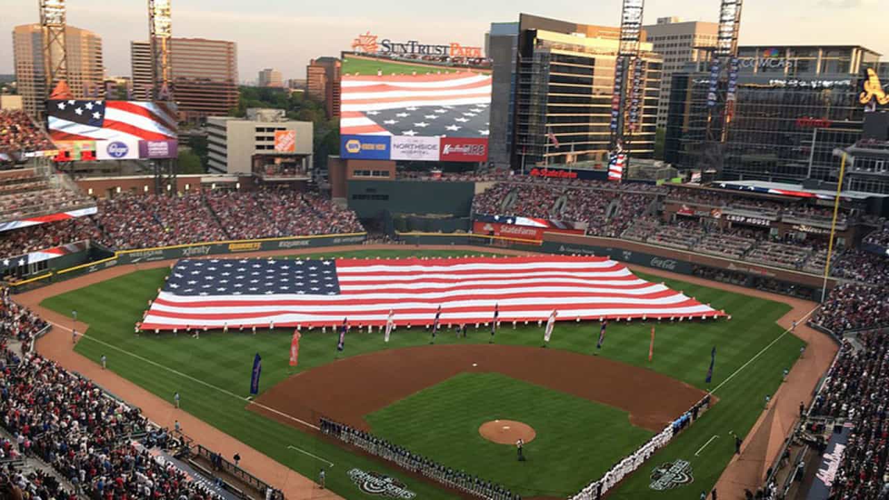 Aerial view of spectators and large American flag displayed over ball park field during baseball game.