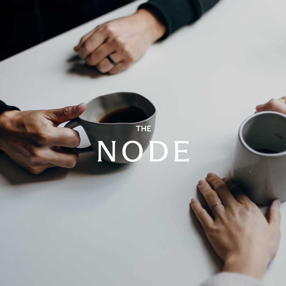 Close-up of table with two pairs of hands holding coffee cups.